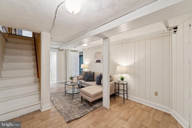 sitting room with a textured ceiling, stairway, baseboards, and light wood-style floors