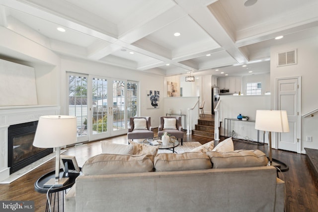 living room with visible vents, dark wood-type flooring, beam ceiling, and a glass covered fireplace