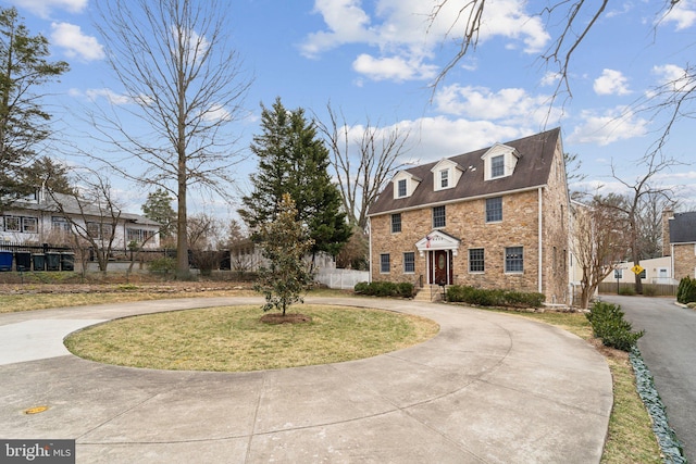 georgian-style home with stone siding, fence, curved driveway, and a front yard