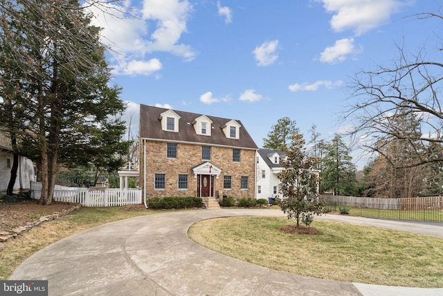 colonial house featuring stone siding, curved driveway, a front lawn, and fence