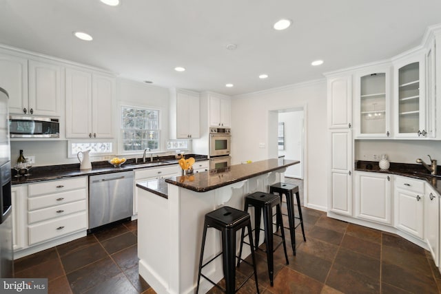 kitchen with appliances with stainless steel finishes, glass insert cabinets, a breakfast bar area, white cabinetry, and a sink