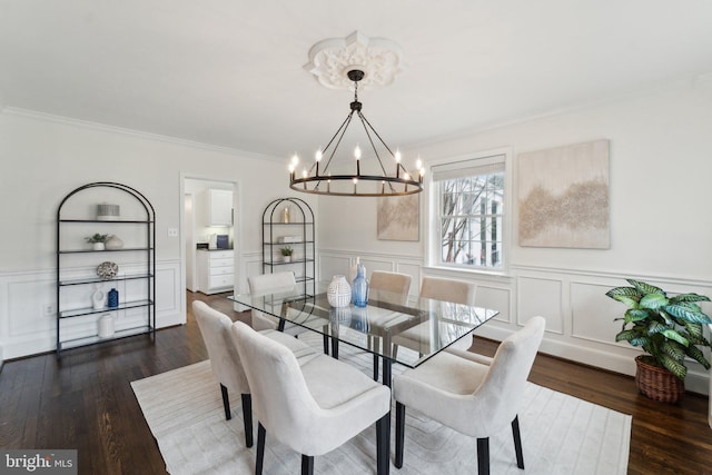 dining room featuring dark wood-style flooring, a notable chandelier, crown molding, and wainscoting