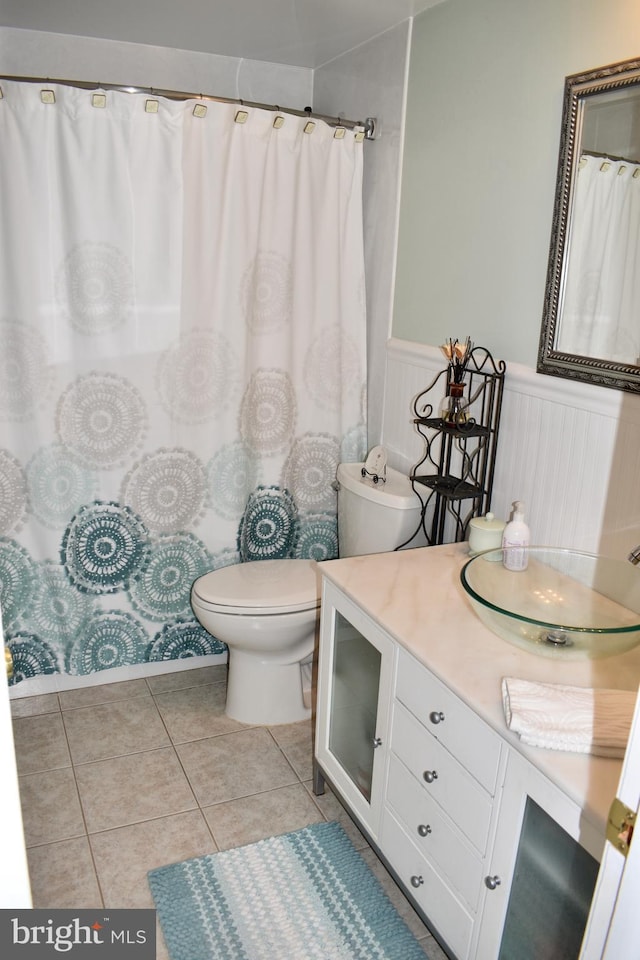 full bath featuring toilet, tile patterned floors, vanity, and wainscoting