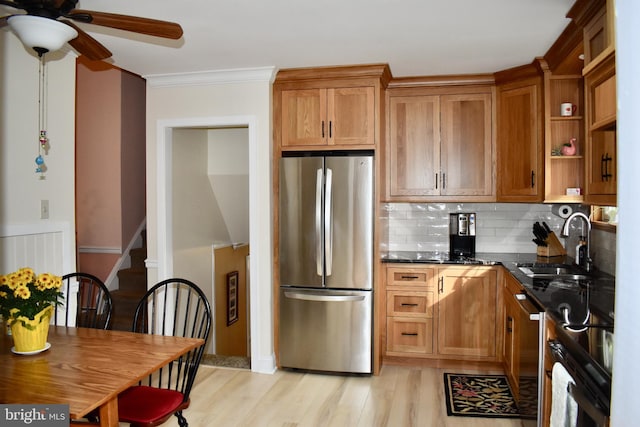 kitchen with brown cabinetry, dark stone countertops, stainless steel appliances, light wood-style floors, and a sink