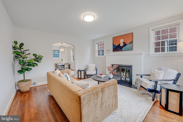 living room featuring plenty of natural light, baseboards, arched walkways, wood finished floors, and a brick fireplace