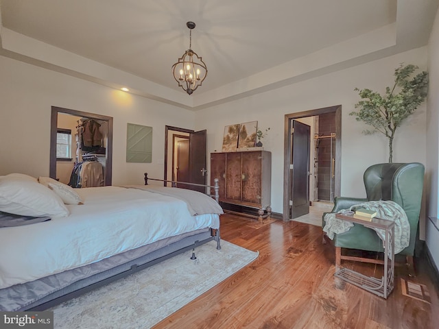 bedroom featuring a notable chandelier, a tray ceiling, and wood finished floors