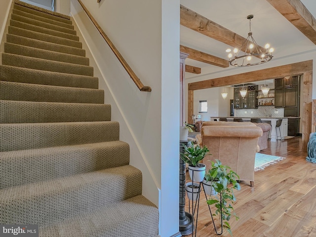 stairway with wood finished floors, beam ceiling, and an inviting chandelier