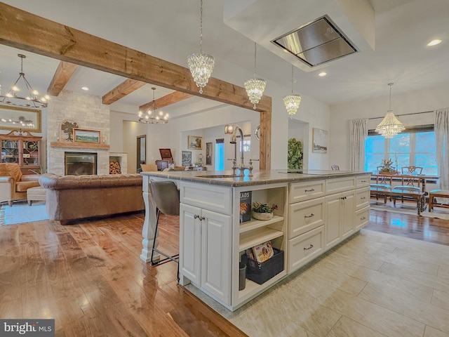 kitchen with a chandelier, a kitchen island with sink, a sink, open floor plan, and pendant lighting