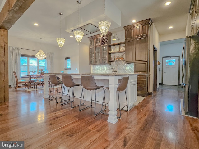 kitchen with a breakfast bar, decorative light fixtures, light countertops, glass insert cabinets, and freestanding refrigerator