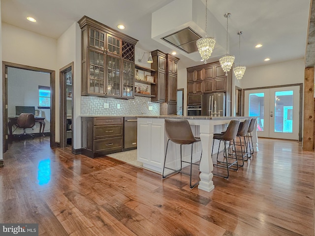 kitchen with dark brown cabinetry, appliances with stainless steel finishes, glass insert cabinets, a center island, and light countertops