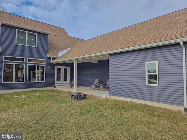 back of property featuring a patio, a fire pit, a yard, french doors, and roof with shingles