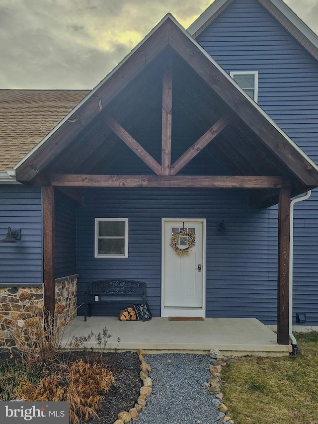 exterior entry at dusk featuring stone siding and a shingled roof