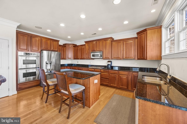 kitchen with a breakfast bar, crown molding, light wood finished floors, stainless steel appliances, and a sink