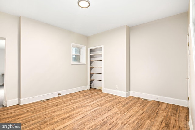 empty room with light wood-type flooring, visible vents, and baseboards