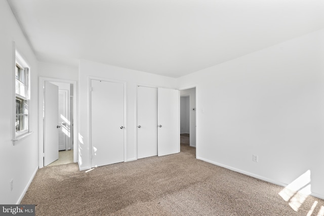 unfurnished bedroom featuring light carpet, baseboards, and two closets