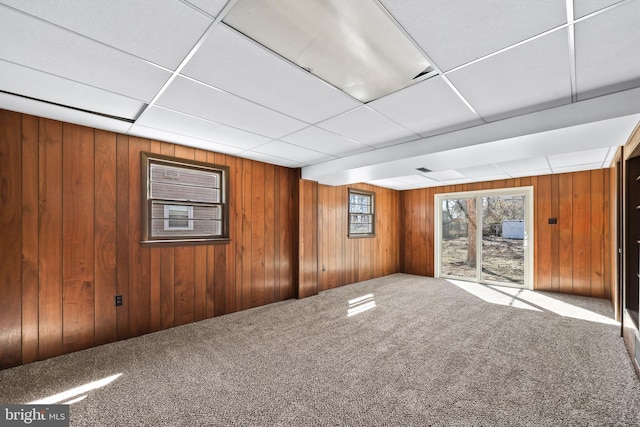 spare room featuring carpet floors, wooden walls, and a paneled ceiling