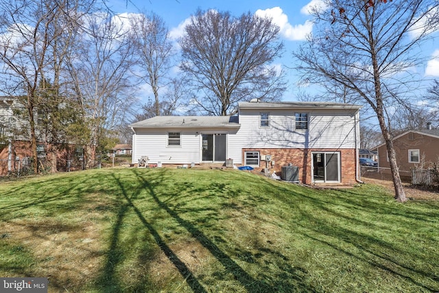 rear view of house with entry steps, brick siding, fence, and a lawn