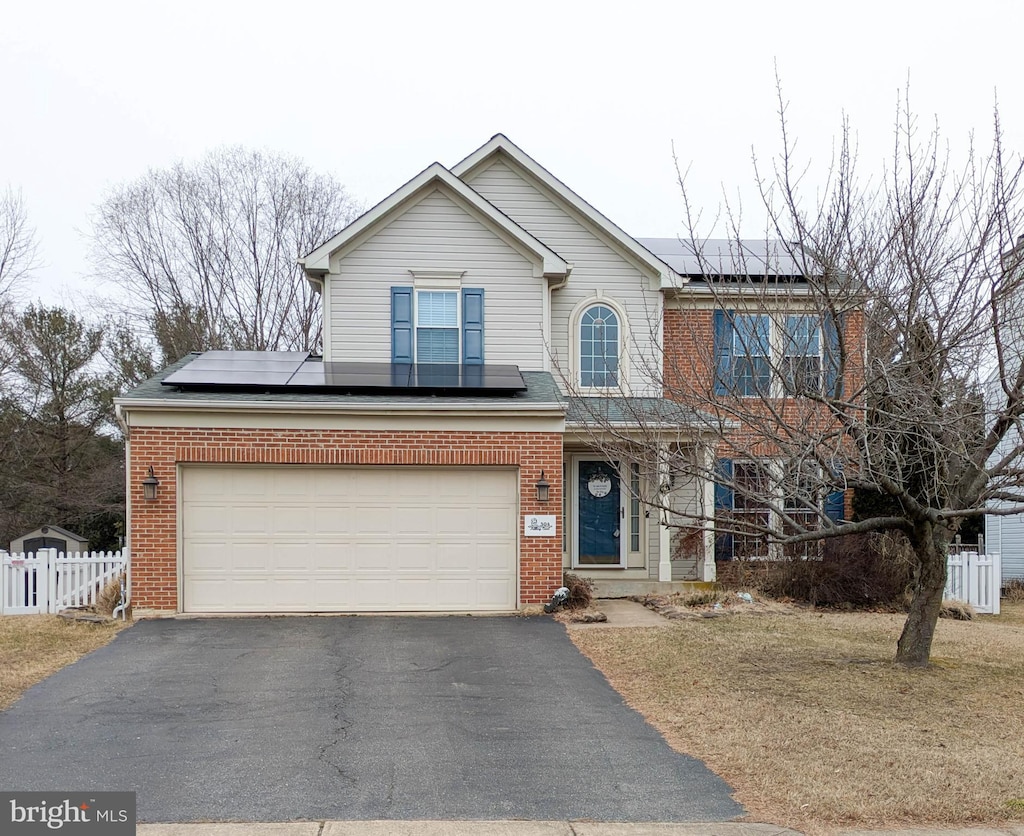 view of front facade with a garage, solar panels, aphalt driveway, fence, and brick siding