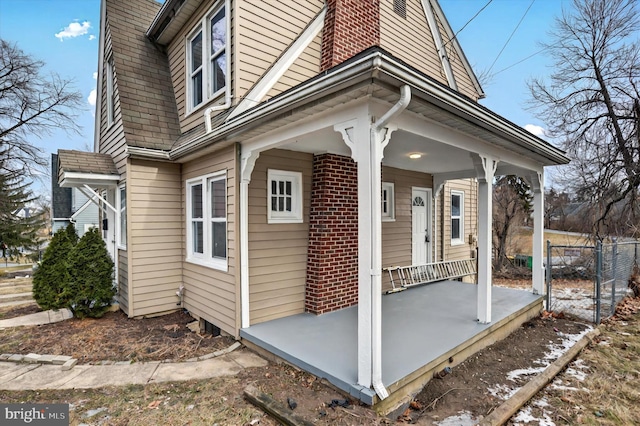 view of side of home featuring a porch, a chimney, and brick siding