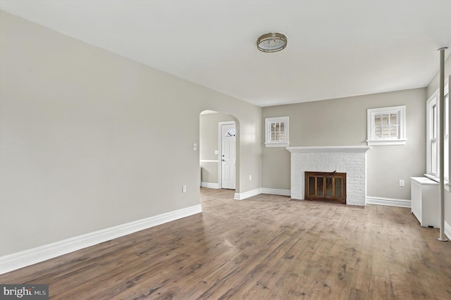 unfurnished living room with arched walkways, a fireplace, wood finished floors, and baseboards