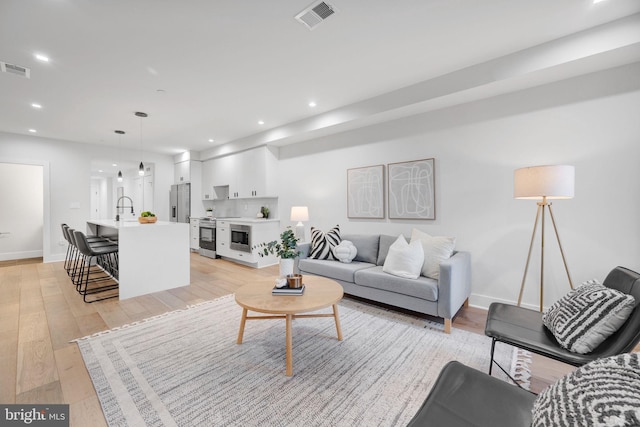 living area with light wood-type flooring, visible vents, baseboards, and recessed lighting