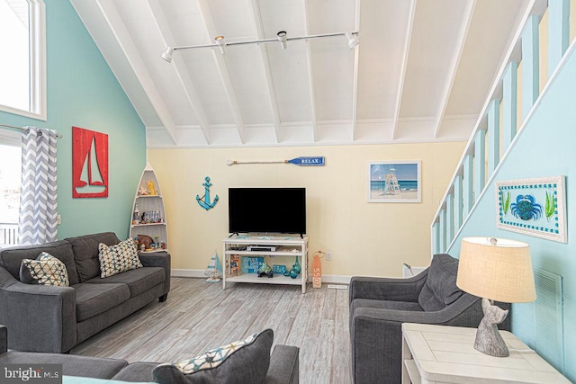 living area featuring beam ceiling, wood finished floors, baseboards, and stairs