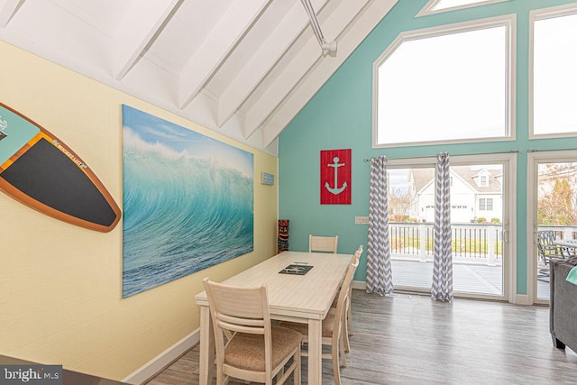 dining area featuring high vaulted ceiling, baseboards, and wood finished floors