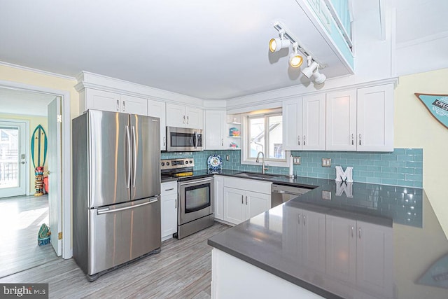 kitchen with a sink, white cabinetry, appliances with stainless steel finishes, backsplash, and dark countertops