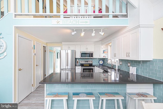 kitchen with stainless steel appliances, a peninsula, a sink, white cabinets, and dark countertops