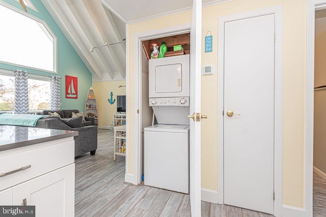 washroom with laundry area, baseboards, light wood finished floors, and stacked washer / drying machine