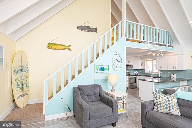 living room with baseboards, stairway, light wood-style floors, high vaulted ceiling, and beam ceiling