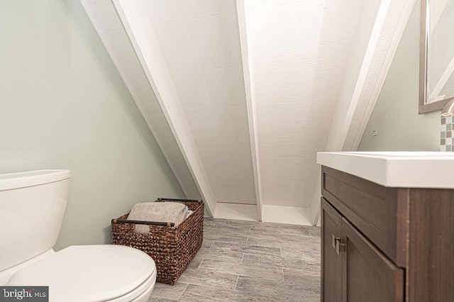 bathroom with toilet, wood finish floors, a tile shower, and vanity