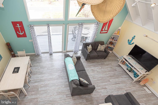 living room featuring visible vents, a high ceiling, baseboards, and wood finished floors