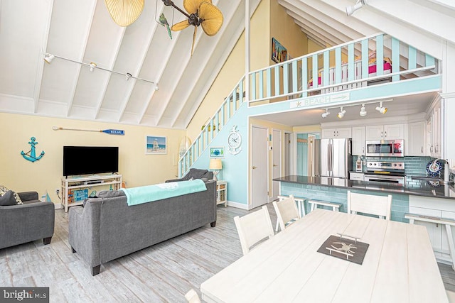 living area with beam ceiling, rail lighting, light wood-style flooring, high vaulted ceiling, and stairs