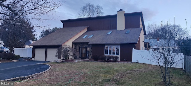 view of front of home featuring aphalt driveway, a garage, fence, a chimney, and a front yard