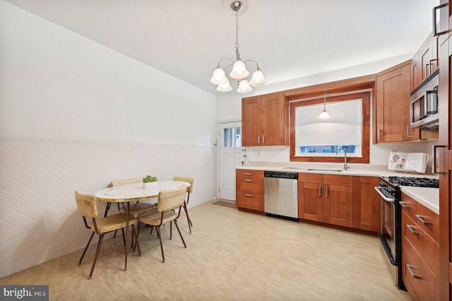 kitchen with a wainscoted wall, stainless steel appliances, light countertops, brown cabinets, and decorative light fixtures