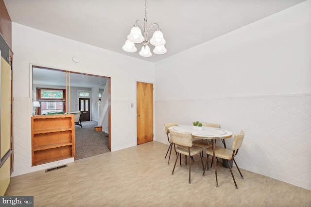 dining room with a chandelier, a wainscoted wall, visible vents, and tile walls