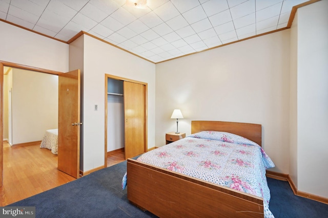 bedroom with ornamental molding, a closet, wood finished floors, and baseboards