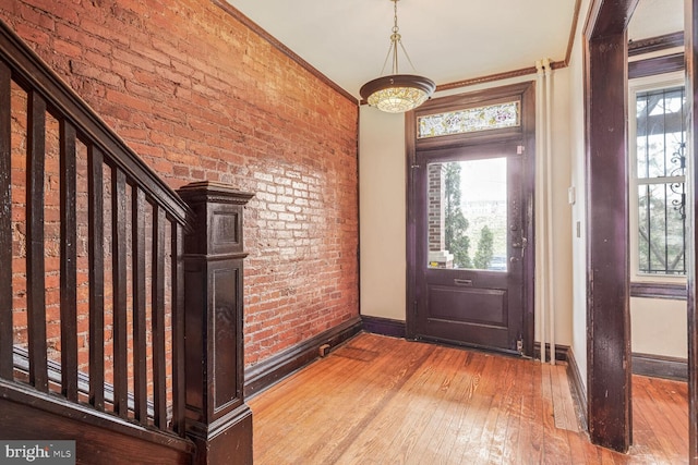 entryway featuring stairs, brick wall, light wood-type flooring, and a wealth of natural light