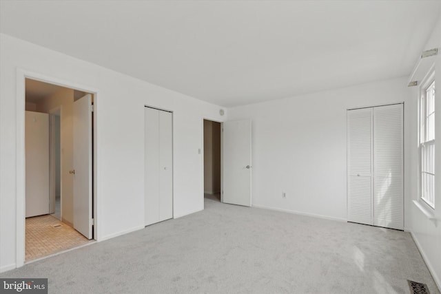 unfurnished bedroom featuring light carpet, two closets, visible vents, and baseboards