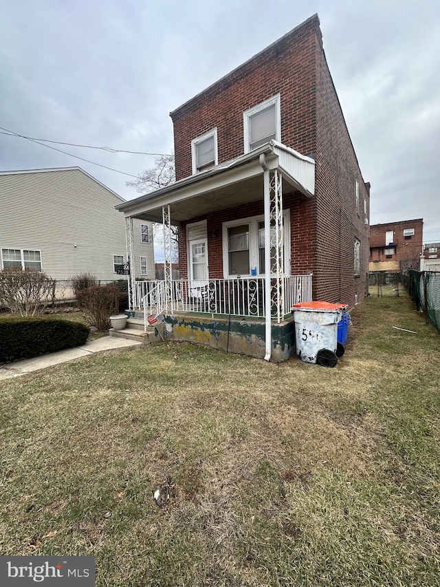 view of front of home with covered porch, brick siding, a front yard, and fence