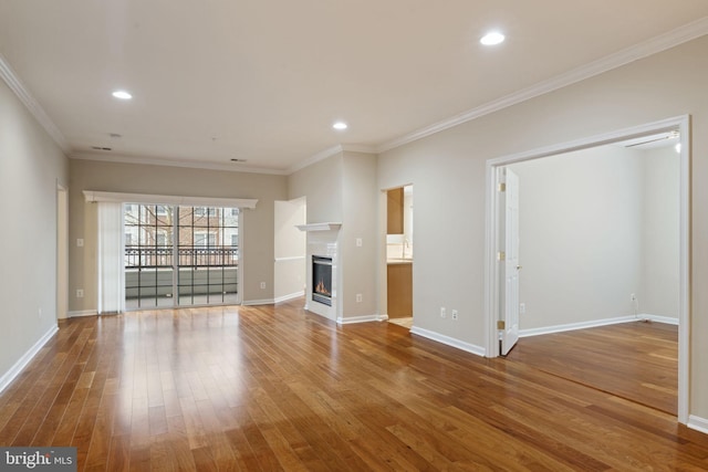 unfurnished living room featuring recessed lighting, wood finished floors, baseboards, ornamental molding, and a glass covered fireplace