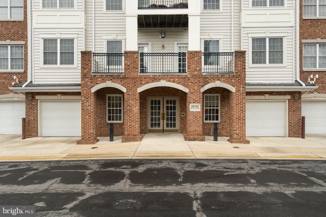 multi unit property with an attached garage, brick siding, driveway, and french doors