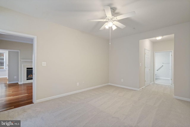 empty room featuring baseboards, a tile fireplace, a ceiling fan, and light colored carpet