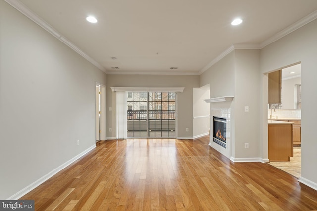 unfurnished living room featuring ornamental molding, light wood finished floors, a tile fireplace, and baseboards