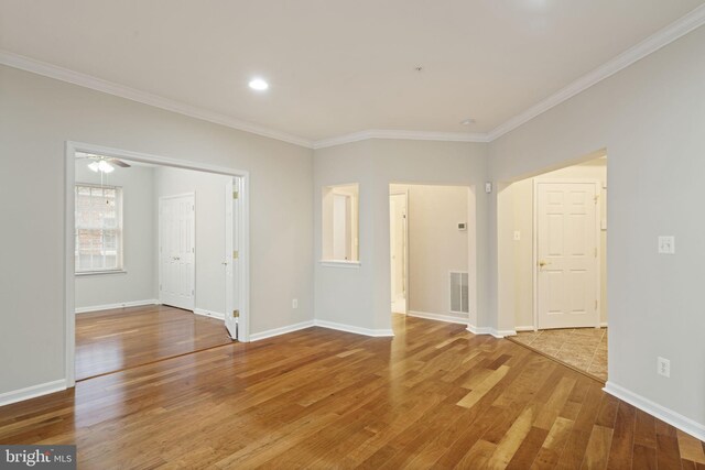 empty room featuring ornamental molding, wood finished floors, visible vents, and baseboards