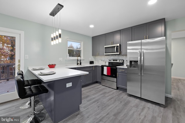 kitchen featuring a breakfast bar area, a peninsula, hanging light fixtures, stainless steel appliances, and light countertops