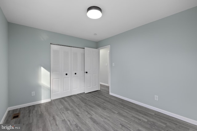 unfurnished bedroom with a closet, wood finished floors, visible vents, and baseboards