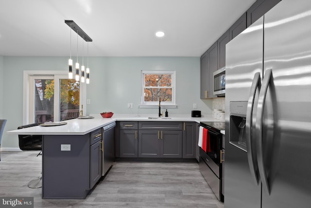 kitchen with a breakfast bar, pendant lighting, light countertops, appliances with stainless steel finishes, and a peninsula