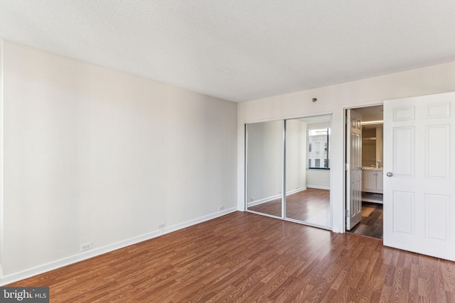 unfurnished bedroom featuring a closet, ensuite bathroom, a textured ceiling, wood finished floors, and baseboards